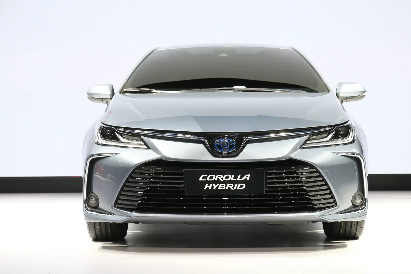 نمای روبه‌روی کرولا هیبرید نقره‌ای مایل به آبی با جلوپنجرهٔ پهن و پلاک COROLLA HYBRID